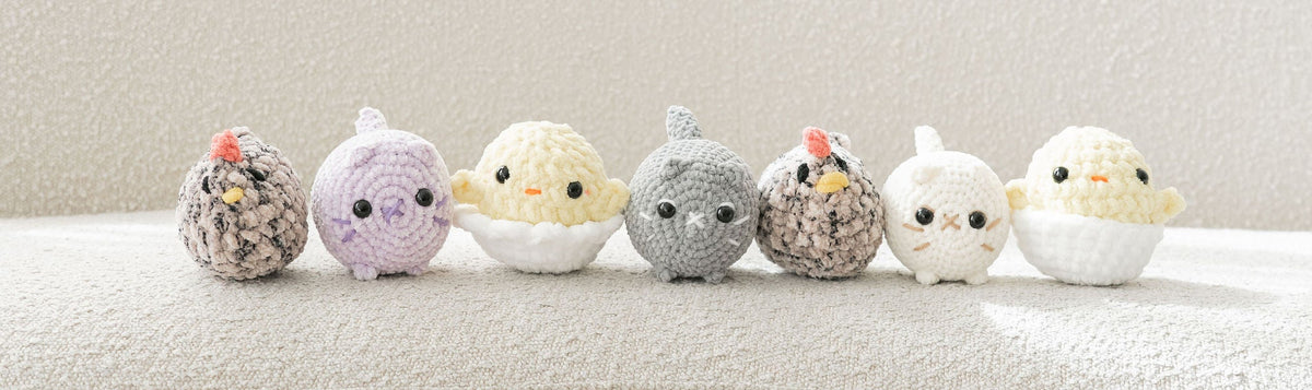 Six small crocheted plush chick toys lined up on a soft cream fabric surface against a bright white background.